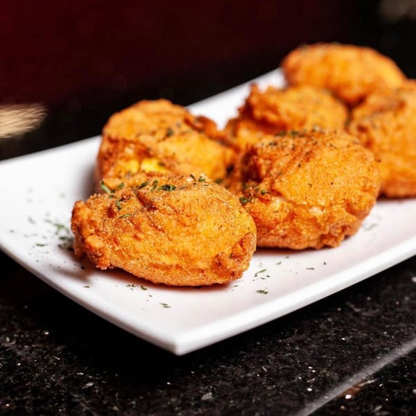 Crispy golden-brown fried appetizers, lightly seasoned with herbs, served on a white rectangular plate.