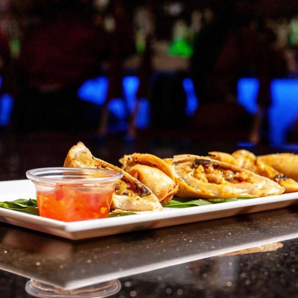 Fried pastries with a red dipping sauce on a white plate, against a dark, blue-lit background.