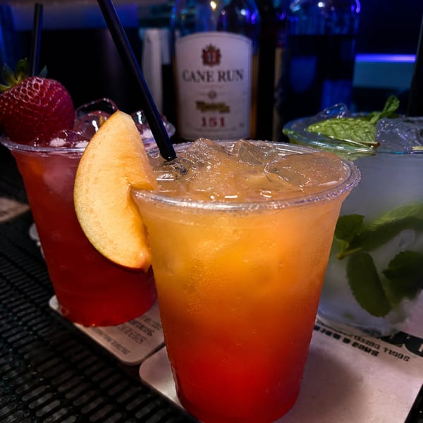 Three vibrant cocktails, including a strawberry-garnished red drink and an orange-red one, on a bar.