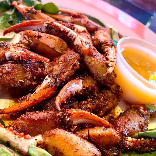 Plate of seasoned crab claws and legs with a side of dipping sauce and greens.