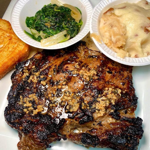 Grilled steak with garlic, mashed potatoes, sautéed spinach, and toast on a white plate.
