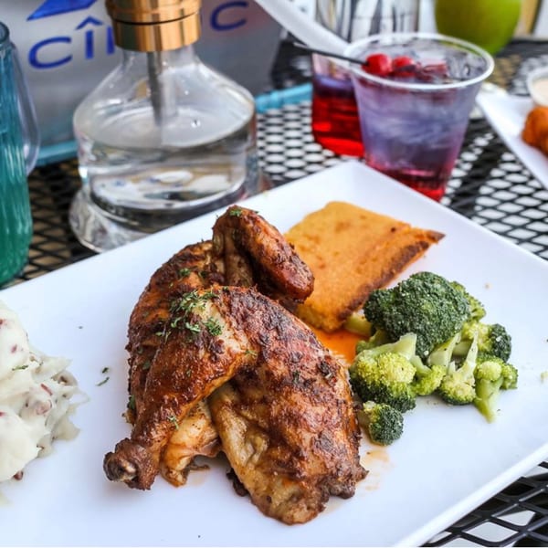 Plate of roasted chicken, mashed potatoes, broccoli, and cornbread with drinks and a hookah.