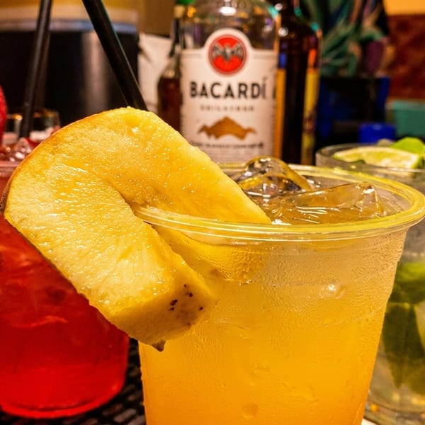 Three colorful cocktails with fruit garnishes and a Bacardi bottle on a bar.